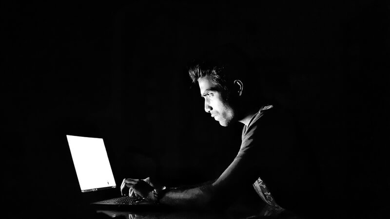 Man working on computer in the dark and performing zero day exploit